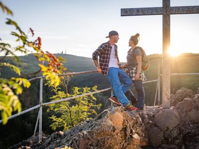 Zwei junge Menschen im Sonnenuntergang auf dem Aschenbergstein (Lauchagrund) am Gipfelkreuz mit Blick in Richtung Großem Inselsberg (Inselsbergregion im Thüringer Wald)