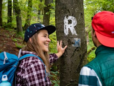Zwei Wanderer stehen vor der Wegemarkierung des Rennsteigs in der Inselsbergregion im Thüringer Wald