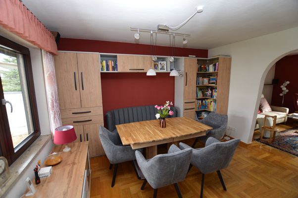 Essbereich mit Holztisch, gepolsterten Stühlen und Wohnwand im Ferienhaus Urban